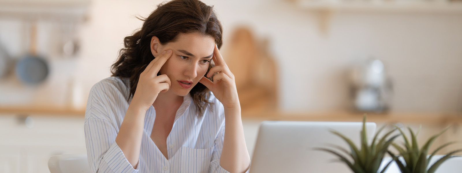 A person is using a telephone while holding a houseplant and looking at a person with a human face in an indoor setting.