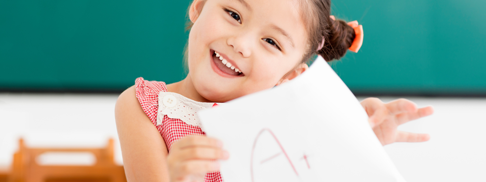 A young girl holding up an A+ test