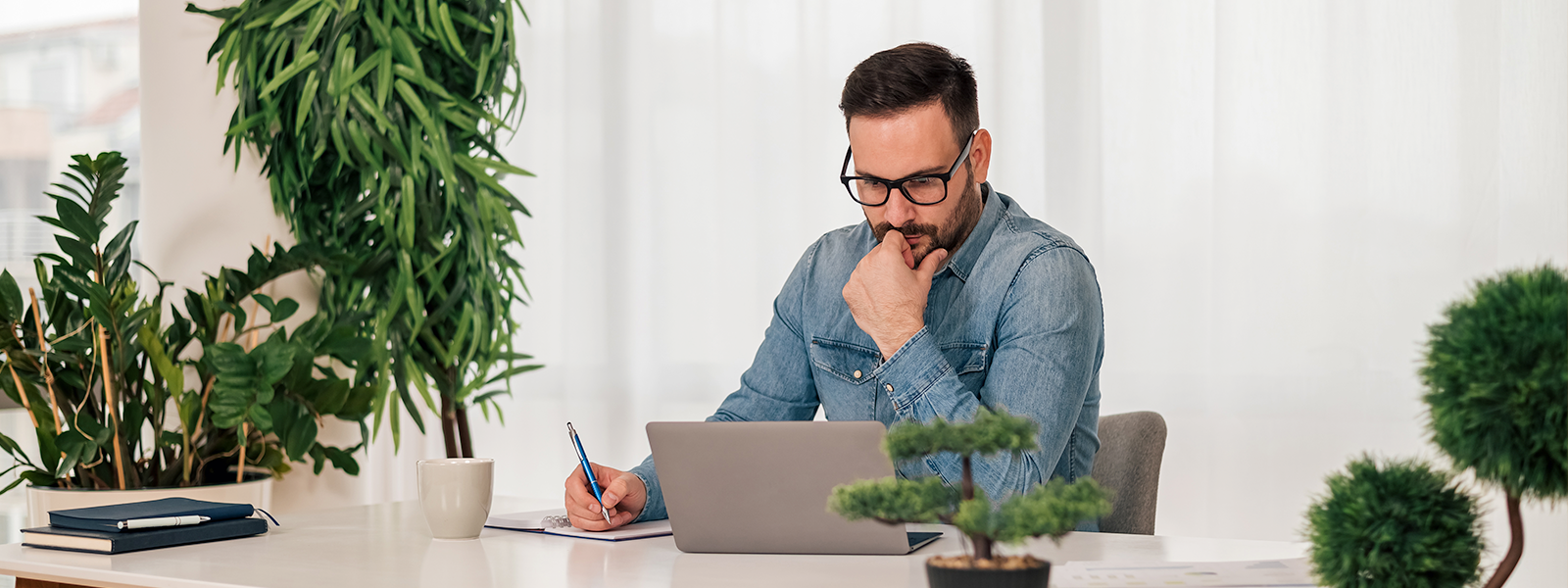 A person sits at a table with a laptop and a pen.