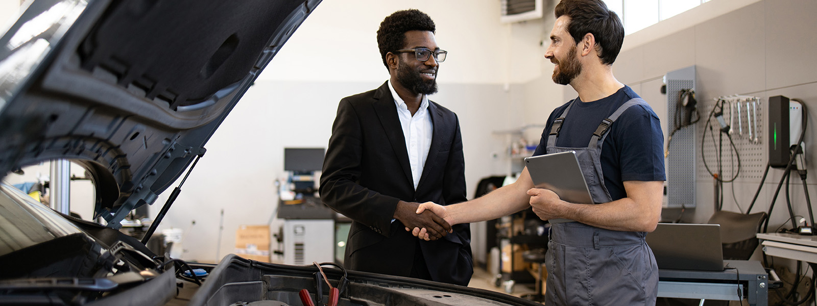 A mechanic and a professional shaking hands in an auto repair shop.