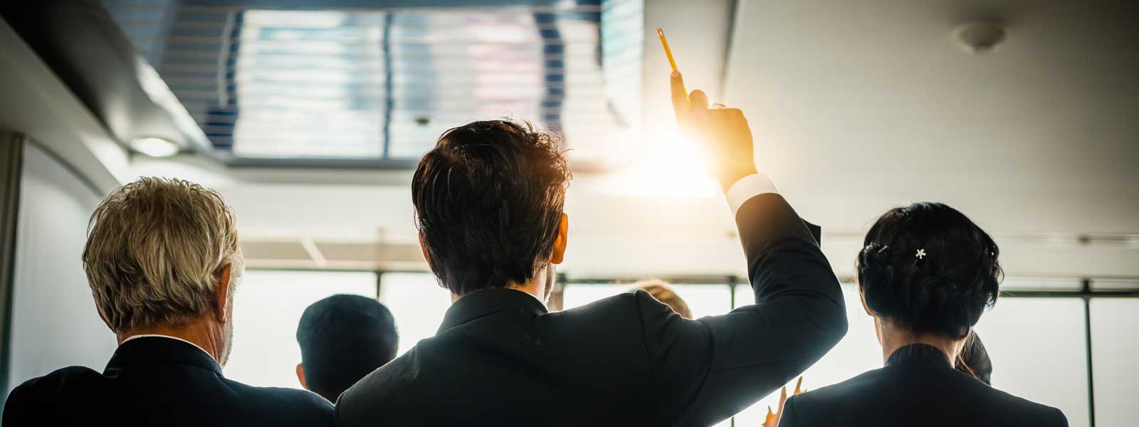 A businessperson raises his hand to speak at a meeting