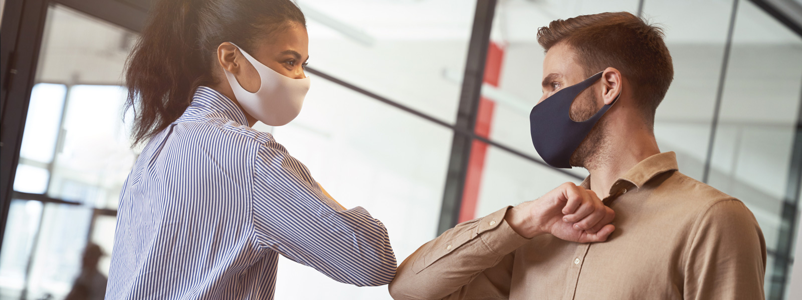 Two masked young professionals bump elbows