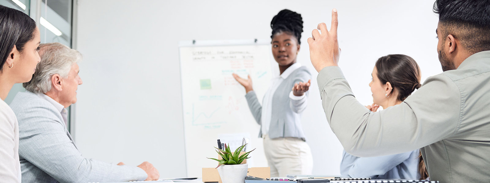 A diverse group of individuals in a meeting room, actively participating by raising their hands.