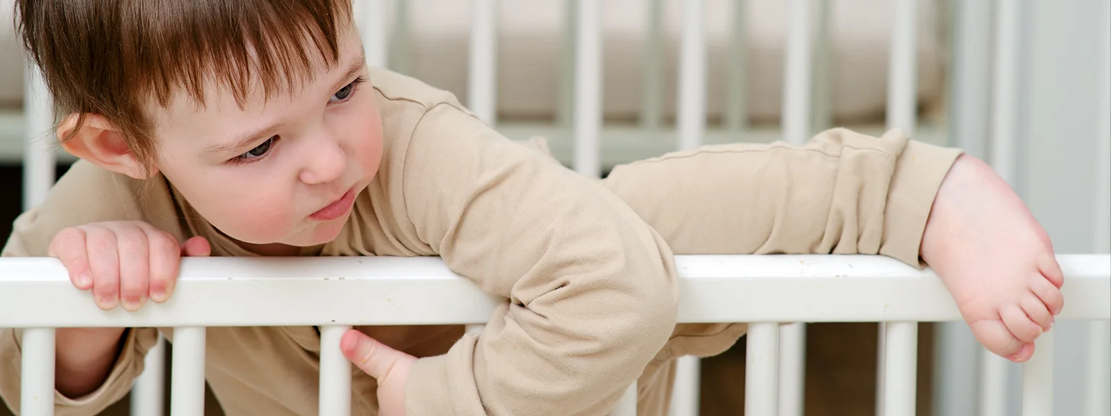 A photo of a child trying to climb out of a crib